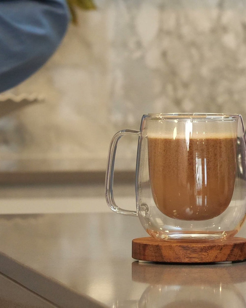 The finished ThyroBase PM drink, a warm cocoa in a glass mug beside the PM pouch.