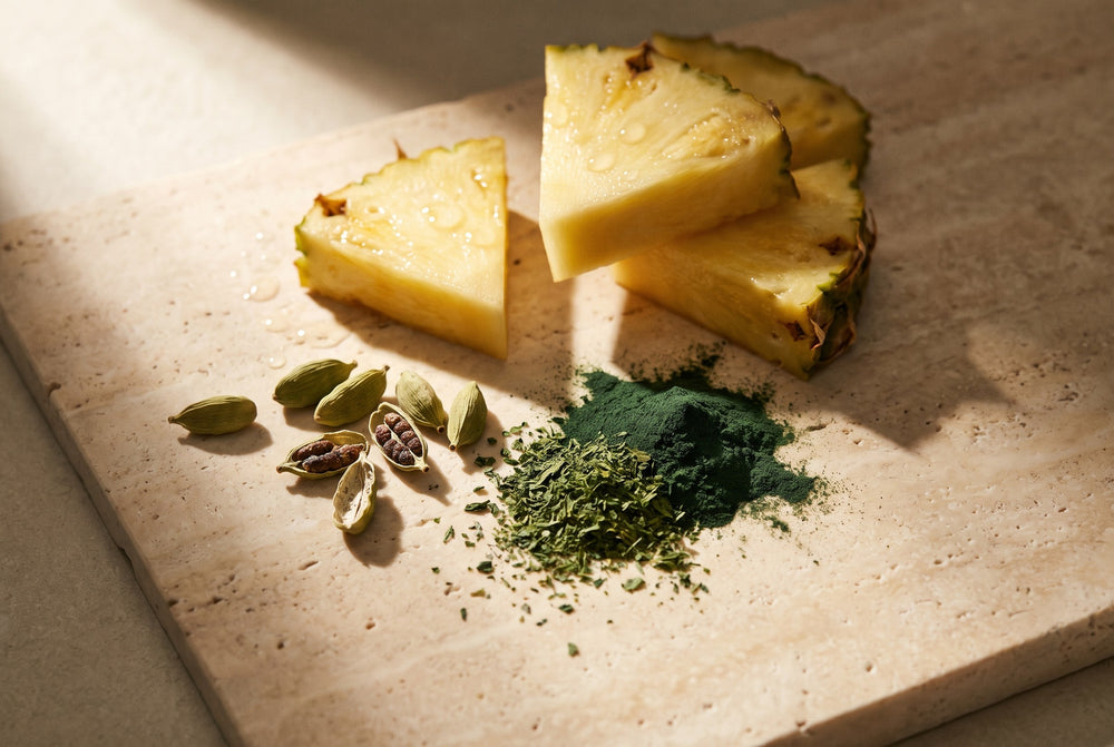 Fresh pineapple, green cardamom pods and spirulina powder on travertine in golden light